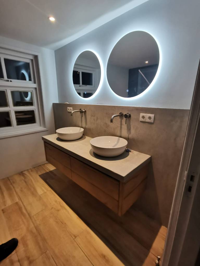 Moderne badkamermeubel met twee waskommen en kranen, verfraaid met twee ronde spiegels erboven.