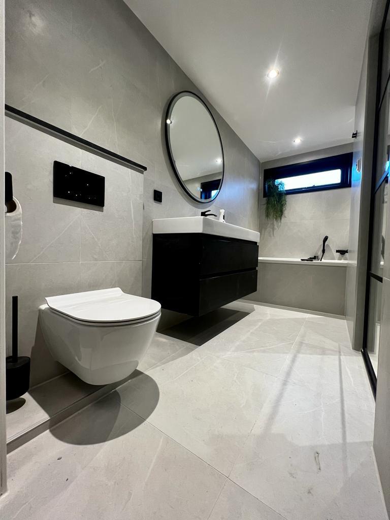 Strakke, modern gerenoveerde badkamer met zwarte elementen zoals kranen, douchekop en accessoires, gecombineerd met een minimalistisch design.
