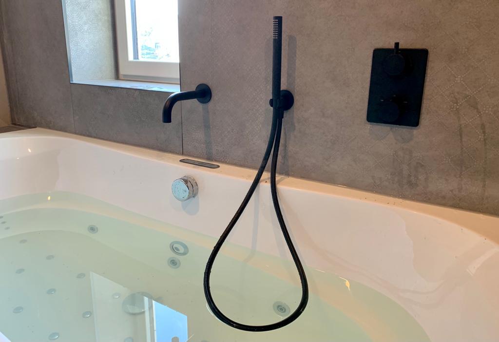 Luxueus bubbelbad met zwarte kranen, geïntegreerd in een stijlvol gerenoveerde badkamer.