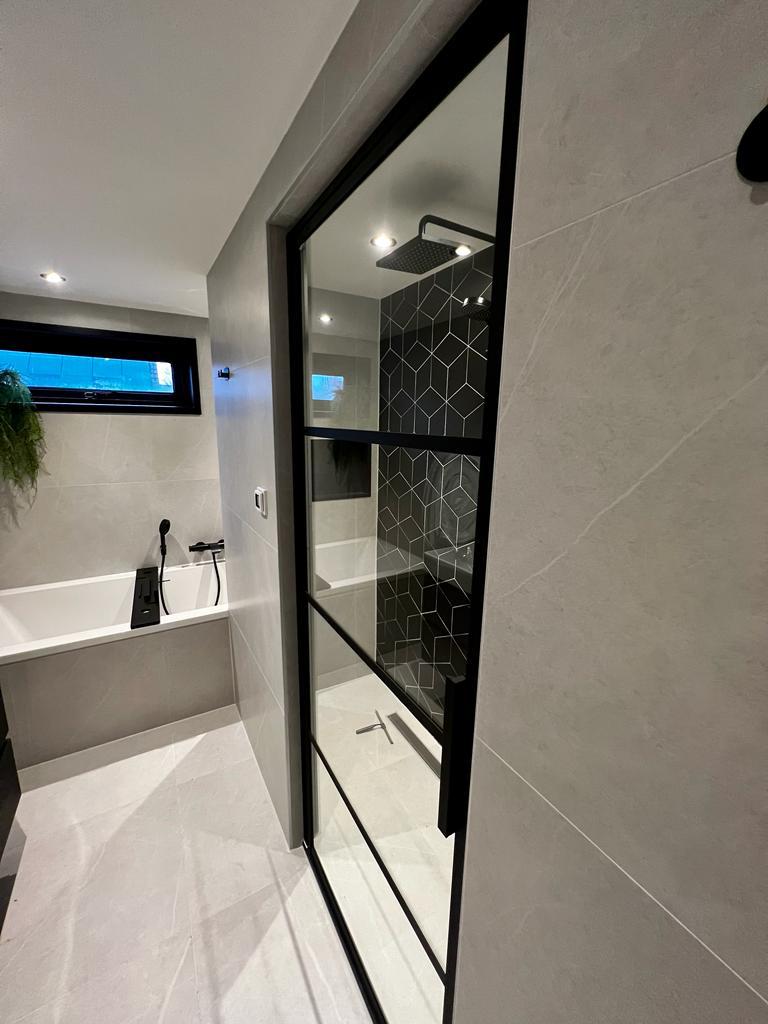 Strak vormgegeven badkamer met zwarte accenten, zoals kranen en accessoires, vastgelegd vanuit een andere hoek om de ruimte en het design te benadrukken.