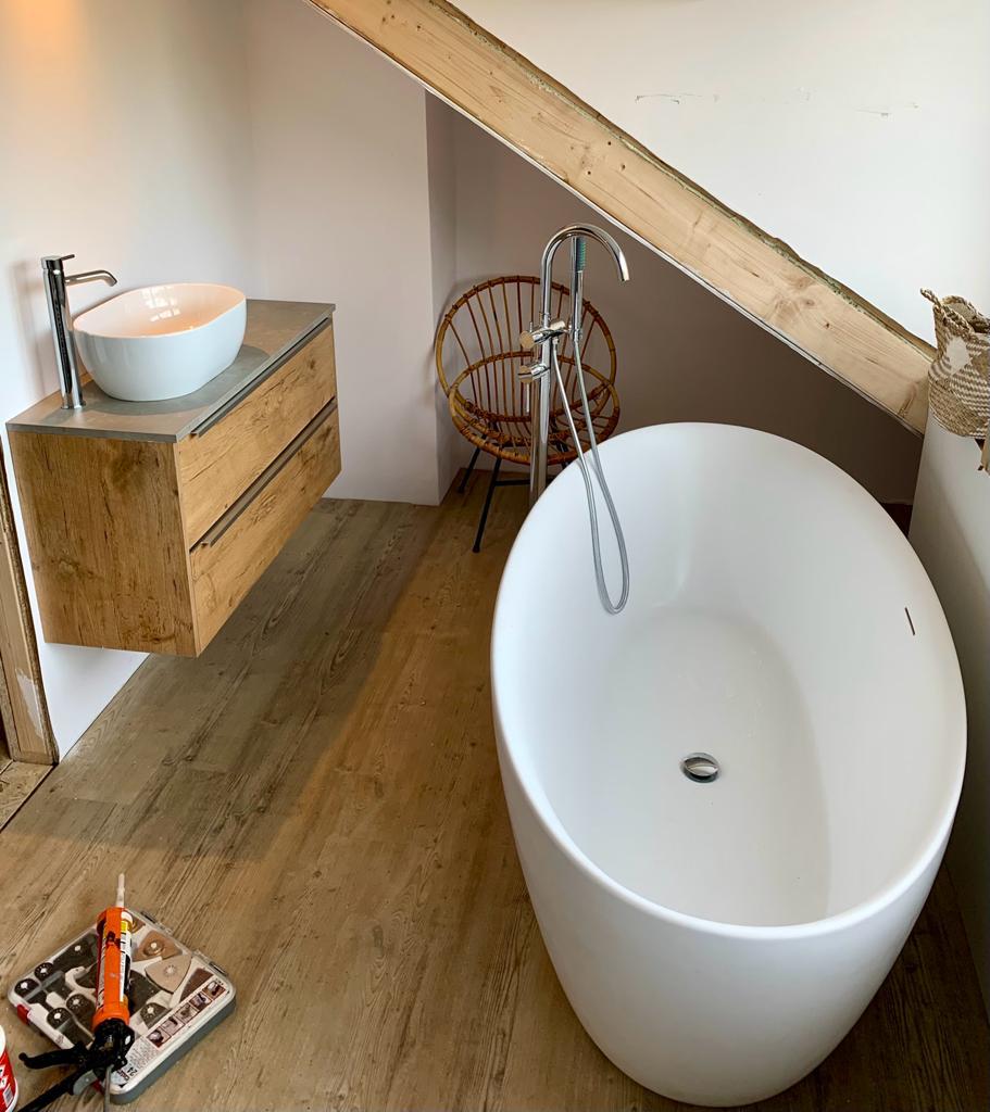 Prachtige kleine ruimte met losstaand bad, gecombineerd met een houten meubel met waskom en bijpassende kranen voor een warme, natuurlijke uitstraling.