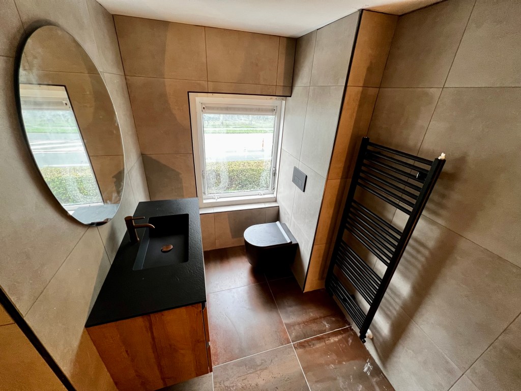 Moderne badkamer met zwarte elementen, waaronder een zwart toilet en een zwarte designradiator, die samen een strakke en stijlvolle uitstraling creëren.