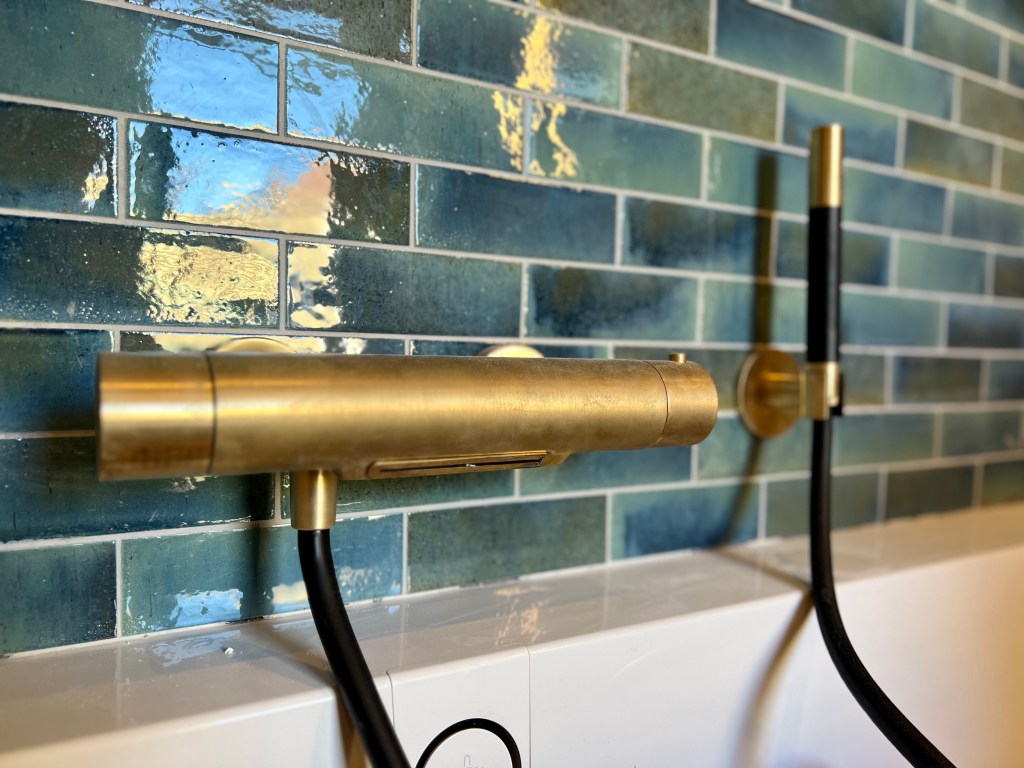 Luxe badkamer met gouden kraan en zwarte details, inclusief een bijpassende douchekop boven een modern bad.