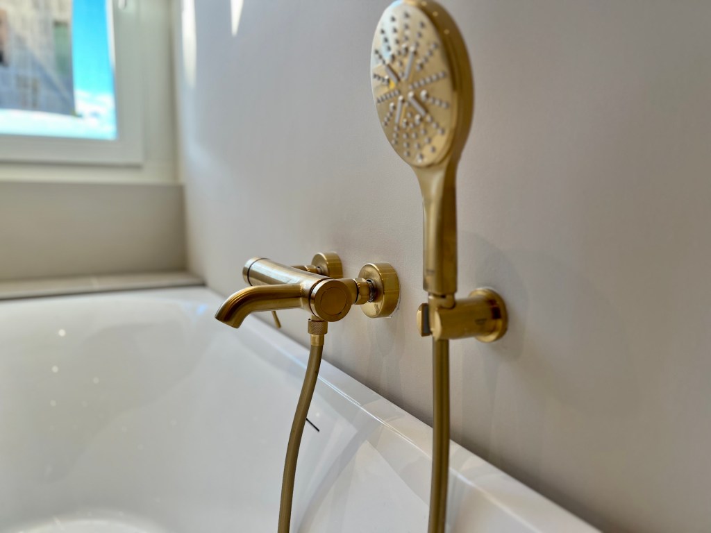 Gouden kraan en douchekop, perfect geplaatst bij het bad voor een luxe uitstraling.