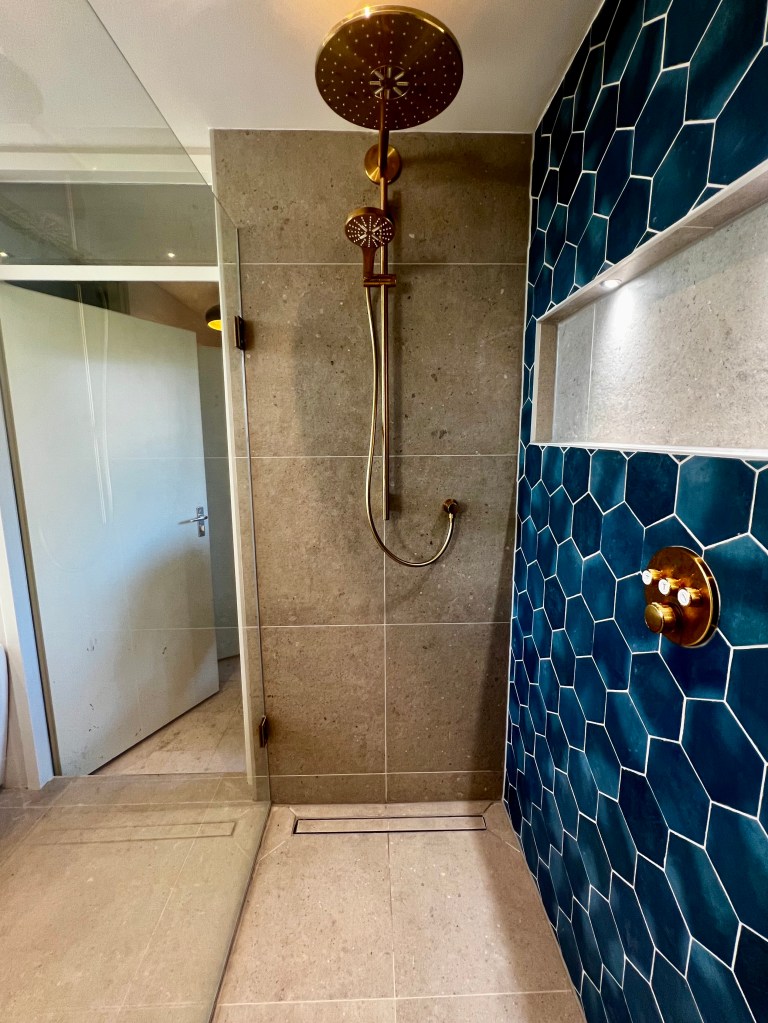 Badkamer met een gouden douchekop, gecombineerd met opvallende blauwe designtegels voor een elegante en kleurrijke uitstraling.