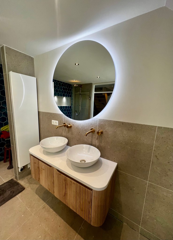 Modern badkamermeubel met twee ronde kommen en kranen, verfraaid met een grote ronde spiegel met ingebouwd licht.