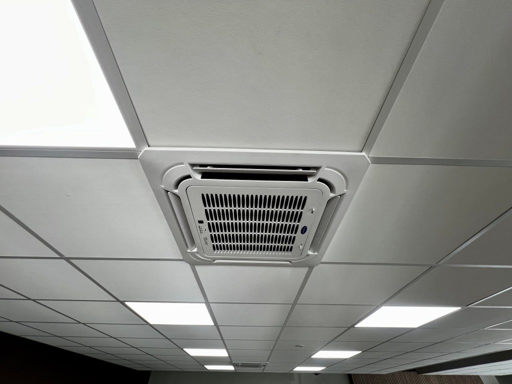 Carrier satelliet unit/cassette airconditioningsysteem, ingebouwd in het plafond van een ruimte. Het ontwerp is strak, met luchtroosters aan de onderkant voor gelijkmatige luchtverdeling in de kamer.