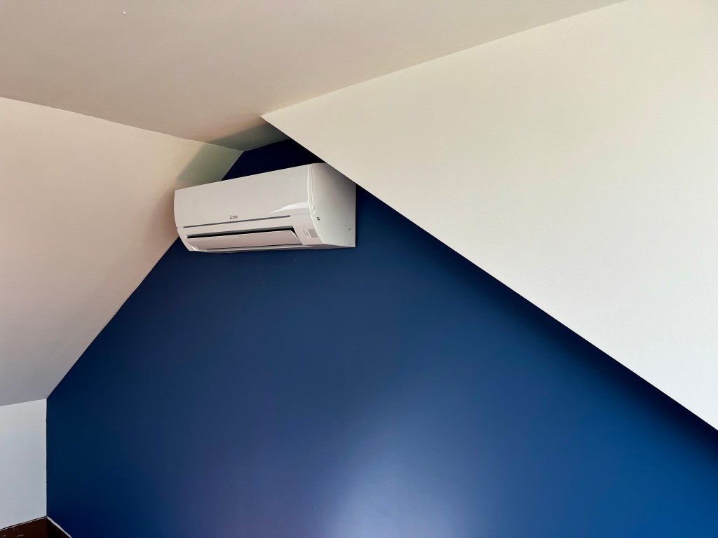Mitsubishi Electric wandunit binnenunit geïnstalleerd tegen een blauwe muur, voor binnenklimaatregeling.
