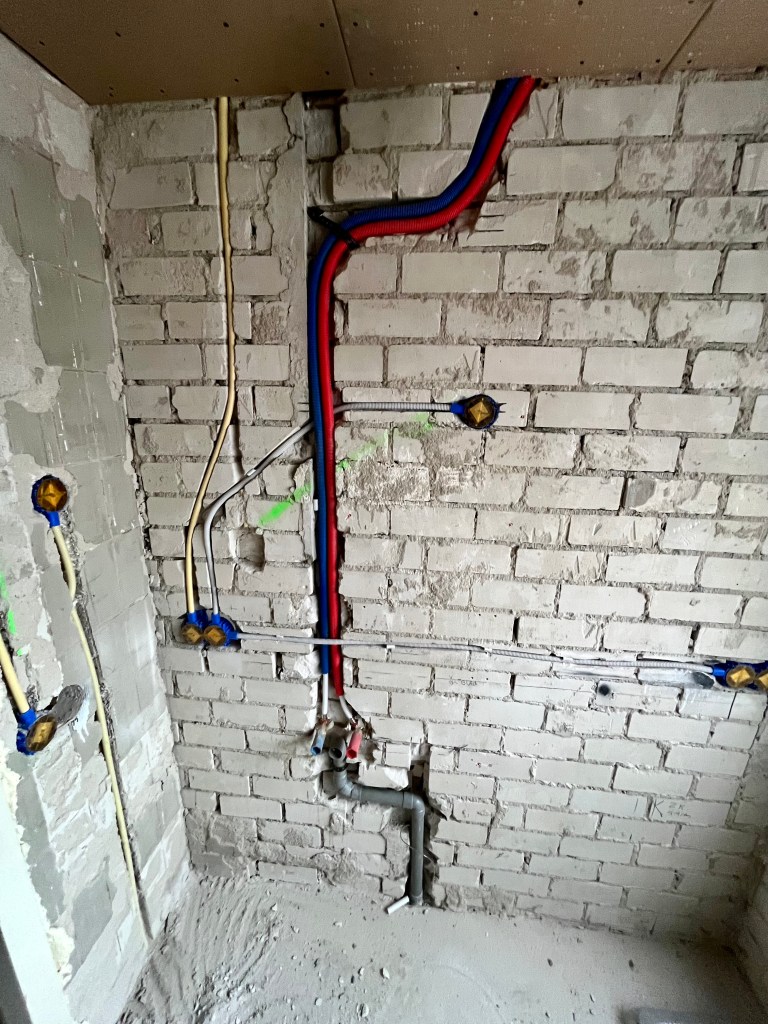 Loodgieterswerkzaamheden voor de wastafel in de badkamer, inclusief warm- en koudwaterleidingen, afvoer en riolering, tijdens badkamerrenovatie.